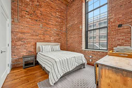 a bedroom with a bed and a brick wall at Riverwalk Apartments, Lawrence, MA