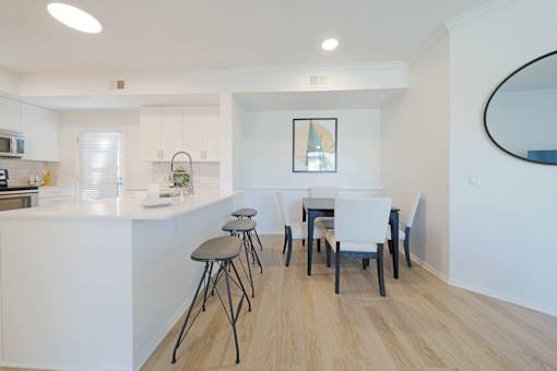 A kitchen with white cabinets and a white island with a bar stool.