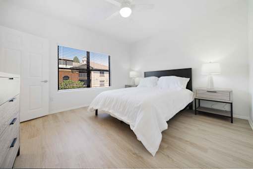 A bedroom with a bed, nightstand, and window with blinds.