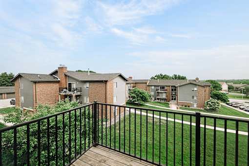 A balcony overlooks a grassy area with apartment buildings in the distance.