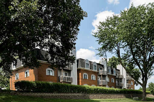 A large building with a red brick exterior and a balcony is surrounded by trees.