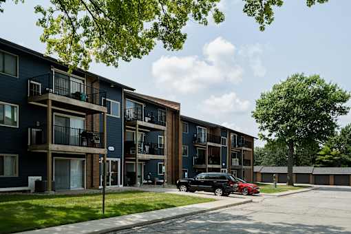 A black car is parked in front of a blue apartment building.