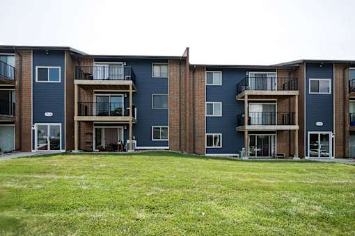 Apartment complex with blue and brown buildings and green grass in front.