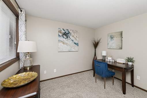 A room with a desk, chair, and two pictures on the wall.