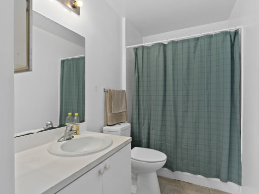 a bathroom with a green shower curtain and a toilet and sink at The Groves at Wimauma Apartments , Florida