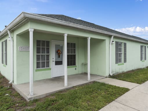 a green house with white pillars and a white door at The Groves at Wimauma Apartments , Wimauma, Florida