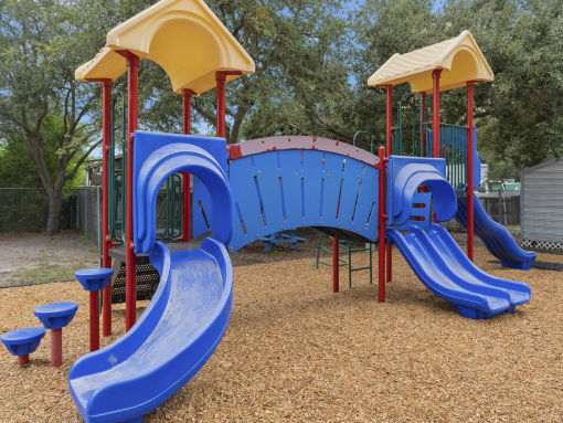 a playground with a blue slide and a yellow and red structure at The Groves at Wimauma Apartments , Florida