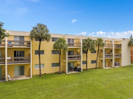 a large yellow apartment building with palm trees in front of it at Cypress Grove, Lauderhill, 33313