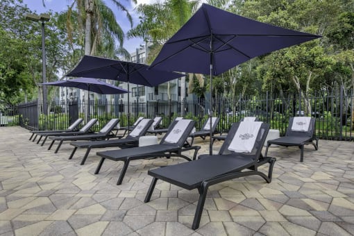 a row of lounge chairs with umbrellas in front of a fence  at Club at Emerald Waters, Hollywood