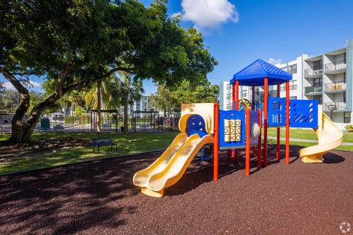 a playground with a slide and monkey bars in front of an apartment building  at Club at Emerald Waters, Hollywood, FL