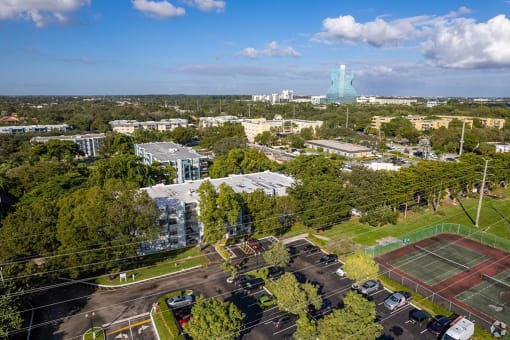 an aerial view of the campus with a tennis court in the foreground and a large building in  at Club at Emerald Waters, Florida