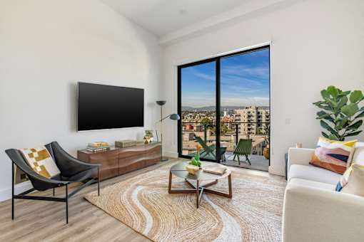 A living room with a black chair, a white sofa, a wooden coffee table, and a large window with a view of the city at WM by CLG, Los Angeles, CA  