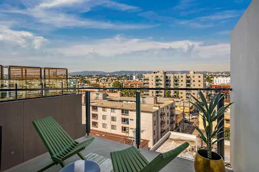 Two green chairs are on a balcony overlooking a cityscape at WM by CLG, Los Angeles California  