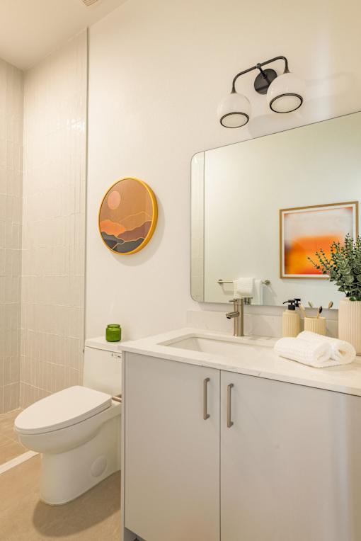 A bathroom with a white toilet, a white sink, a mirror, and a painting on the wall at WM by CLG, California, 90232