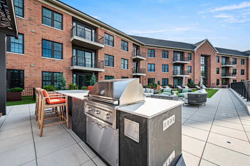 A modern outdoor kitchen setup is placed on a patio in front of a brick apartment building.