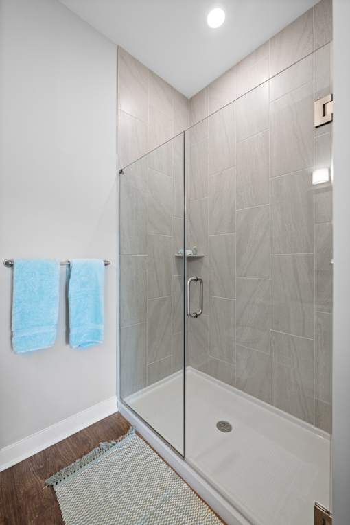 A stand-up shower with a frameless door and modern tile walls in a bathroom with hardwood-style flooring.