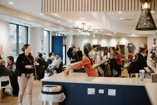 A woman in a red shirt is standing at a counter in a busy room.