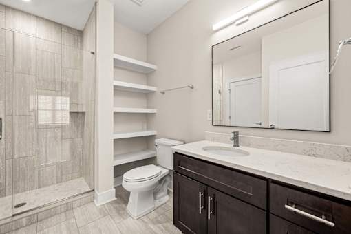 A bathroom with a toilet, sink, and shelves.