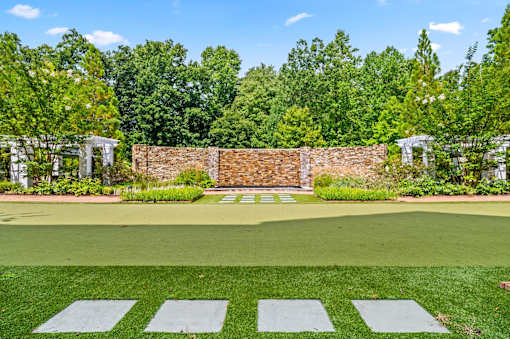A green lawn with a brick wall and trees in the background.