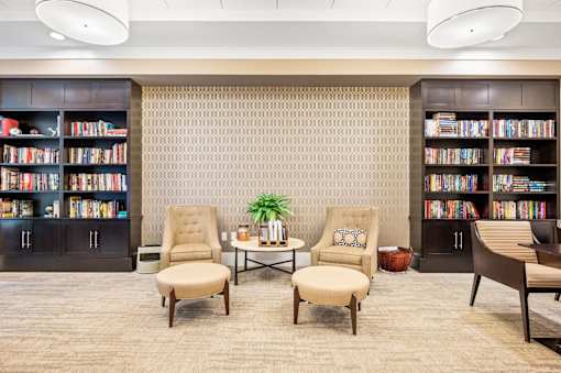 A room with a carpeted floor, two chairs, a table, and bookshelves filled with books.