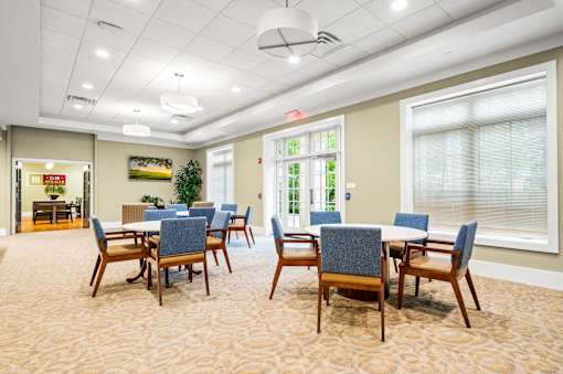 A room with a table and chairs in the foreground and a window with blinds in the background.
