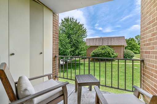 A covered balcony with two chairs, a small table, and two doors leading to a storage closet in an Aspen floor plan at New Kent Apartments, West Chester, PA