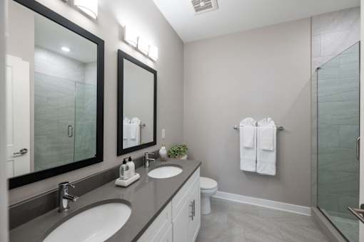 Luxury apartment bathroom featuring quartz countertops, a dual-vanity setup, frameless glass shower doors, and an oversized soaking tub at Claremont on the Square in Exton.