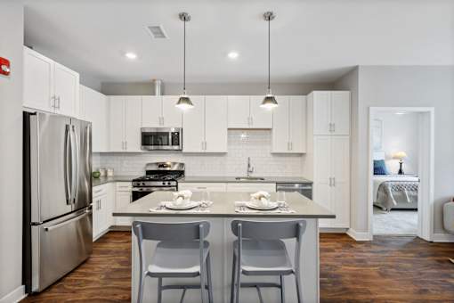 Modern luxury apartment kitchen featuring an oversized island, stainless steel appliances, gas range, quartz countertops, and light contemporary finishes at Claremont on the Square in Exton.