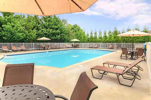 A gated resort-style pool at our Severgn Apartments in Exton, PA with lounge chairs, tables, and umbrellas surrounded by trees.