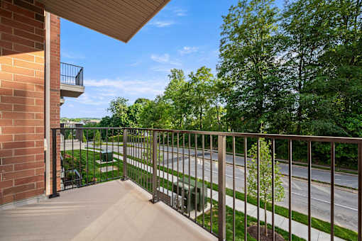 A balcony with a metal railing overlooks a street and greenery.
