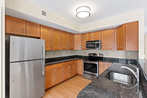 A U-shaped kitchen with stainless steel appliances, granite countertops, modern wooden cabinets, and hardwood-style flooring.