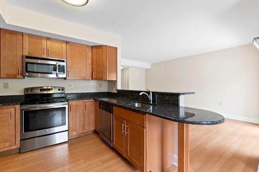 A kitchen with hardwood-style floors, black granite countertops, beautifully-designed breakfast bar, and stainless steel appliances.