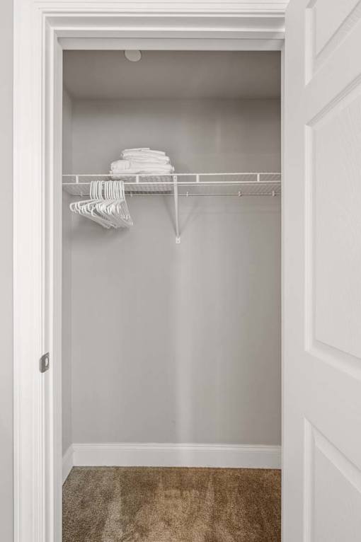A white closet with clothes hanging on a rod.