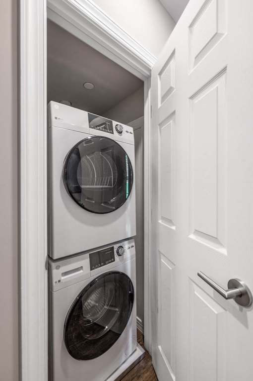A white door is open to reveal a white washer and dryer stacked on top of each other.