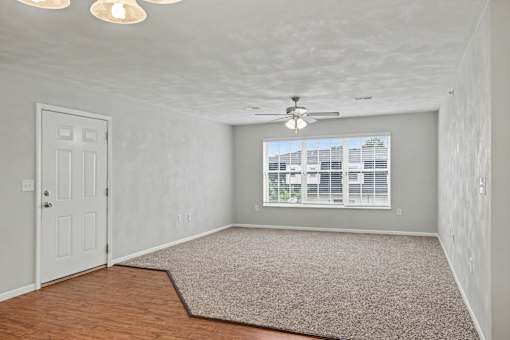 Northbrooke Commons living room with ceiling fan, plush carpeting, and large windows with blinds.