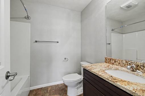 Northbrooke Commons bathroom with large mirror, granite countertop, dark cabinetry, toilet and tub/shower