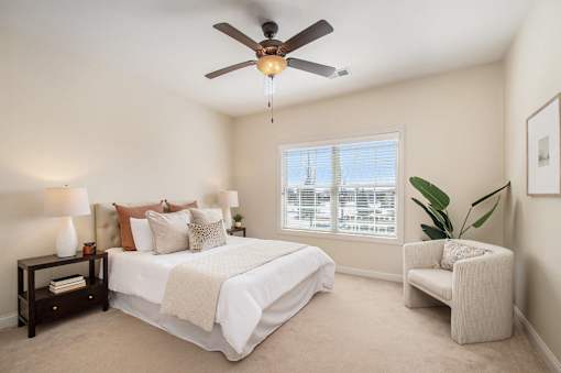 A bedroom with a bed, chair, and ceiling fan.