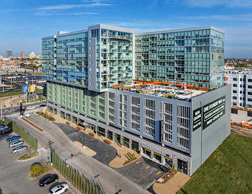 A modern glass building with a parking lot in front. at One Foundry Way Apartments, Missouri