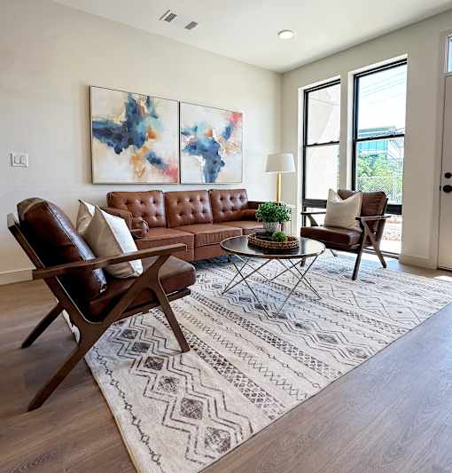A living room with a brown leather couch, a brown chair, and a patterned rug.
