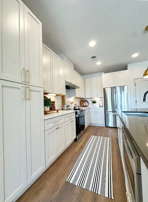 A kitchen with white cabinets and a striped rug on the floor.