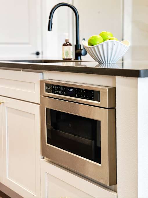 A modern kitchen with a stainless steel oven and a bowl of green apples on the counter.