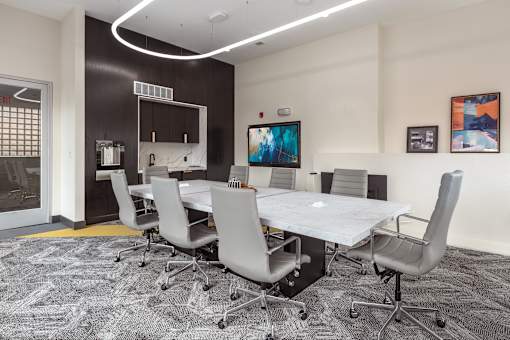 A conference room with a white table and grey chairs.