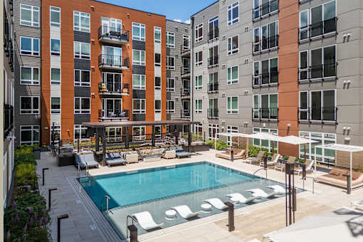 A swimming pool surrounded by lounge chairs and umbrellas in front of apartment buildings.
