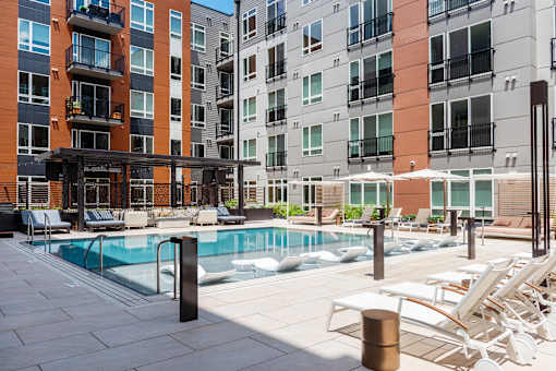 A pool area with sun loungers and a building in the background.