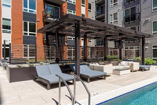 A pool area with a pergola and lounge chairs.