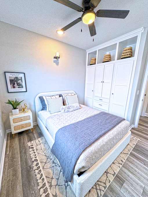 A bedroom with a bed, a ceiling fan, and a cabinet with baskets on top.