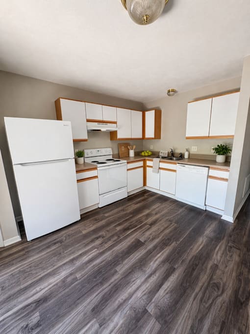 A kitchen with white appliances and wooden floors.