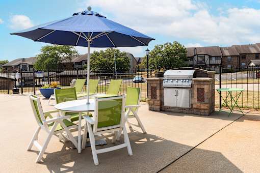 a patio with a table and chairs with an umbrella and a grill