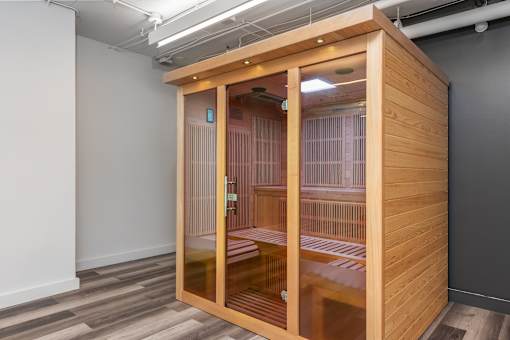 A wooden pod with glass doors is in a room with grey walls.