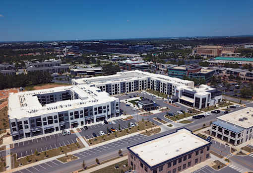 A large white building with a flat roof is surrounded by other buildings and roads.